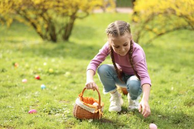 Easter celebration. Cute little girl hunting eggs outdoors, space for text