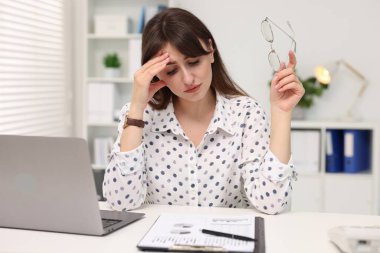 Overwhelmed woman sitting at table with laptop in office