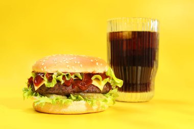 Lezzetli köfteli hamburger ve sarı arka planda soda.