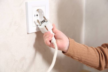 Küçük çocuk elektrik priziyle oynuyor ve kapalı mekanda fişi takıyor, yakın plan. Tehlikeli bir durum.