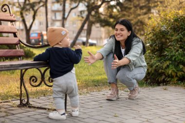 Küçük bebek parkta annesine ilk adımlarını atıyor, arkasını görüyor. Mutlu aile onu arıyor.