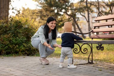 Küçük bebek parkta annesine ilk adımlarını atıyor, arkasını görüyor. Mutlu aile onu arıyor.