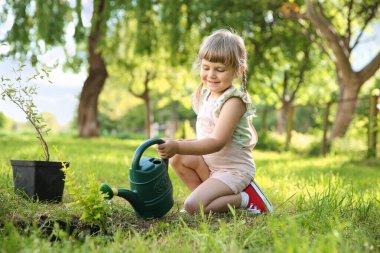 Cute little girl watering tree in garden