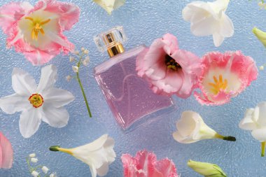 Parfüm ve çiçek dekoru açık mavi plastik yüzeyde, düz yerde.