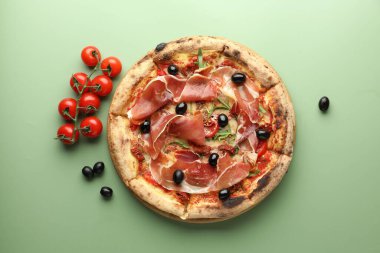 Tasty pizza with cured ham, olives and tomatoes on green background, top view