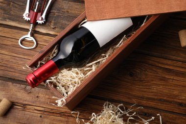 Box with wine bottle, corkscrew and corks on wooden table, flat lay