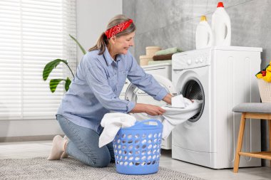 Happy housewife putting laundry into washing machine at home