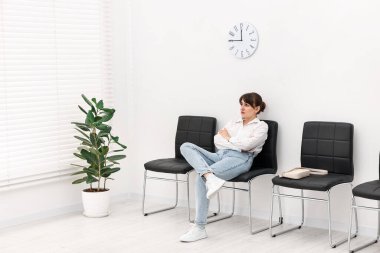 Kadın sandalyede oturuyor ve içeride randevu bekliyor.