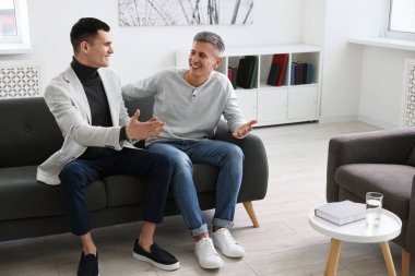 Happy men talking while sitting on sofa at home