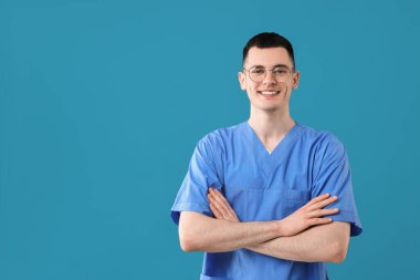 Portrait of smiling medical assistant with crossed arms on light blue background. Space for text