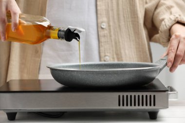 Vegetable fats. Woman pouring cooking oil into frying pan on stove, closeup
