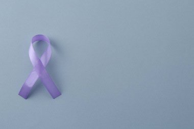 Violet awareness ribbon on light blue background, top view. Space for text