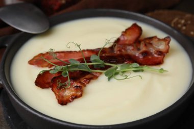 Delicious potato soup with bacon and microgreens in bowl served on table, closeup