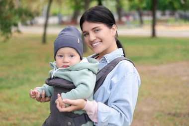 Anne çocuğunu park yerinde (bebek taşıyıcısı) tutuyor.