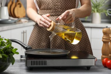 Vegetable fats. Woman pouring cooking oil into frying pan on stove in kitchen, closeup