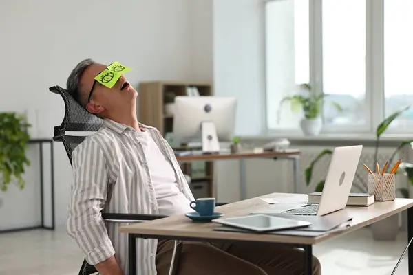 stock image Man with fake eyes painted on sticky notes snoozing at workplace in office