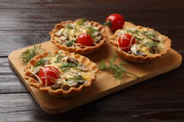 Peynirli, domatesli, mantarlı ve ahşap masadaki dereotlu turtalar.