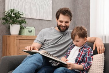 Dad and son reading book together on sofa at home