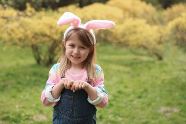 Easter celebration. Cute little girl with bunny ears outdoors, space for text
