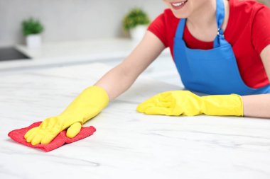 Woman cleaning white marble table with rag in kitchen, closeup