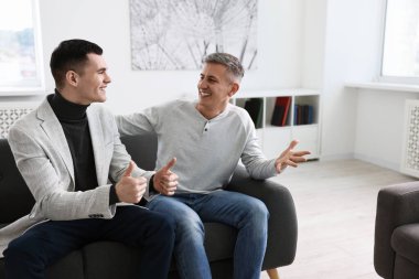 Happy men talking while sitting on sofa at home