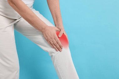 Açık mavi arka planda dizinde ağrıdan muzdarip bir kadın, yakın plan. Metin için boşluk