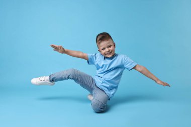 Mutlu küçük çocuk açık mavi arka planda dans ediyor