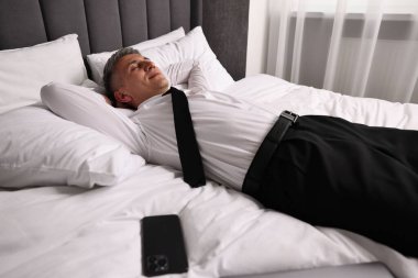 Businessman in office clothes resting on bed indoors