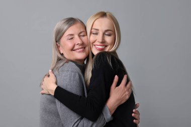 Family portrait of young woman and her mother on grey background