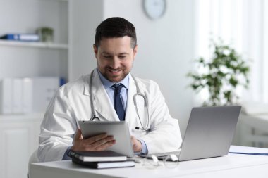 Gülümseyen doktor, klinikteki masada tabletle online danışmanlık yapıyor.