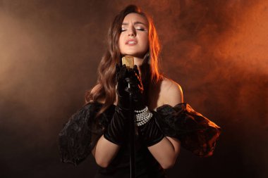 Mikrofonlu güzel genç bir kadın. Renkli ışıklar ve dumanlar içinde şarkı söylüyor.