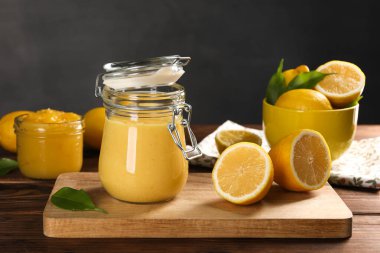 Cam kavanozlarda lezzetli limon ezmesi, taze narenciye meyveleri ve ahşap masada yeşil yapraklar.