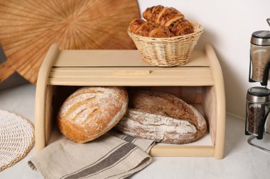 Tahta ekmek sepeti, taze pişmiş somunlar ve mutfaktaki beyaz mermer masada kruvasanlar.