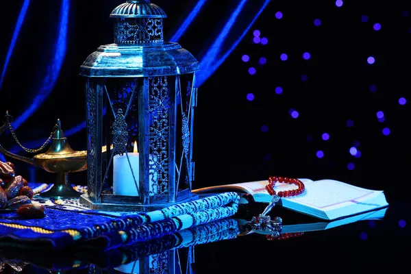 stock image Arabic lantern, Quran, misbaha, Aladdin magic lamp, dates and folded prayer mat on mirror surface against blurred lights at night. Space for text