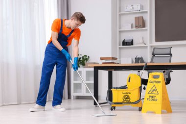 Temizlik servisi. Ofiste yerleri paspasla silen bir adam.
