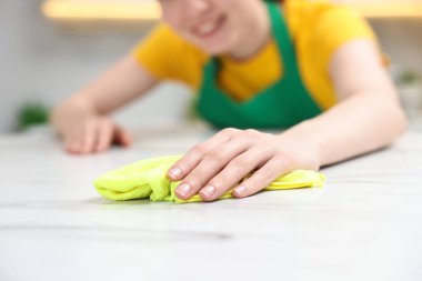 Woman cleaning white marble table with rag in kitchen, closeup