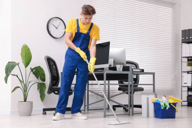 Temizlik işçisi ofiste paspas ve malzeme kovasıyla yerleri yıkıyor.