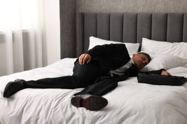 Businessman with briefcase sleeping on bed indoors