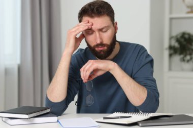 Overwhelmed man with glasses at table indoors