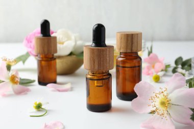 Aromaterapi. Temel yağlar ve çiçekler beyaz masada, yakın plan.