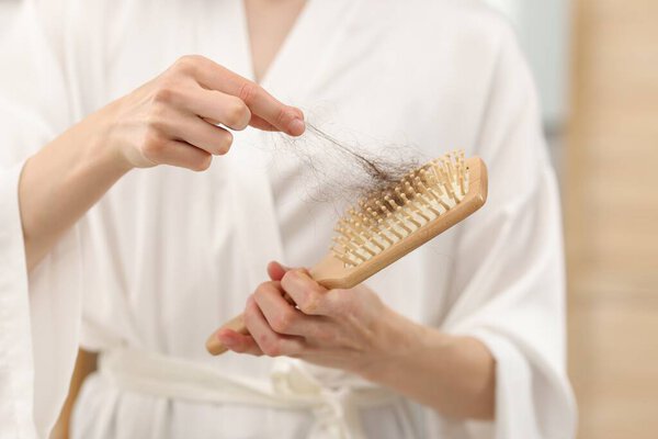 Женщина забирает потерянные волосы из расчёски дома, крупным планом. Задача об алопеции