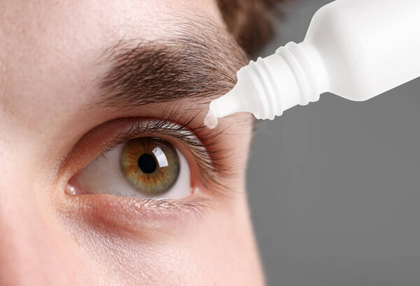 Man applying eye drops on grey background, closeup