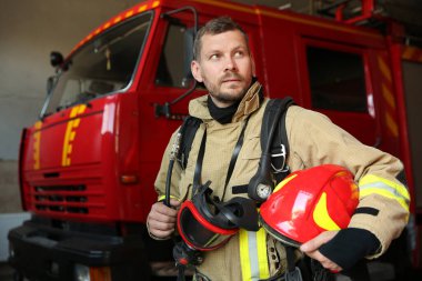 Kasklı ve maskeli itfaiyeci kırmızı itfaiye aracının yanında.