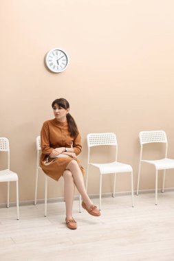 Kadın sandalyede oturuyor ve içeride randevu bekliyor.