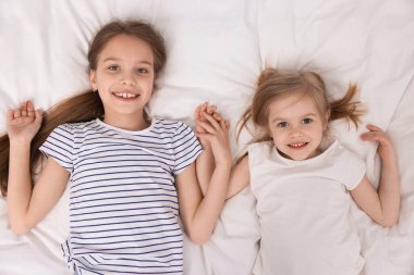 Yatakta sevimli küçük kız kardeşler, üst manzara.