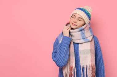 Beautiful woman in warm scarf and hat on pink background, space for text