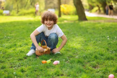 Easter celebration. Cute little boy hunting eggs outdoors, space for text