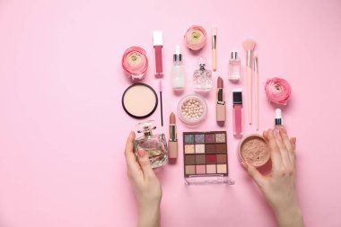 Woman with different makeup products and beautiful spring flowers on pink background, top view. Space for text