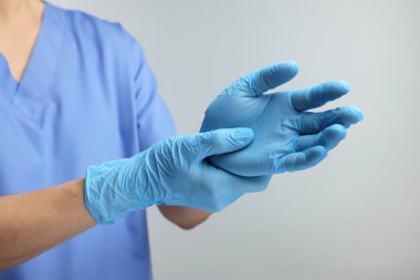 Gri arka planda açık mavi tıbbi eldiven giyen doktor, yakın plan.