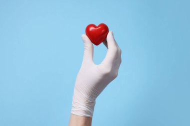 Dekoratif kalbi açık mavi arka planda tutan beyaz tıbbi eldiven giyen doktor, yakın plan.